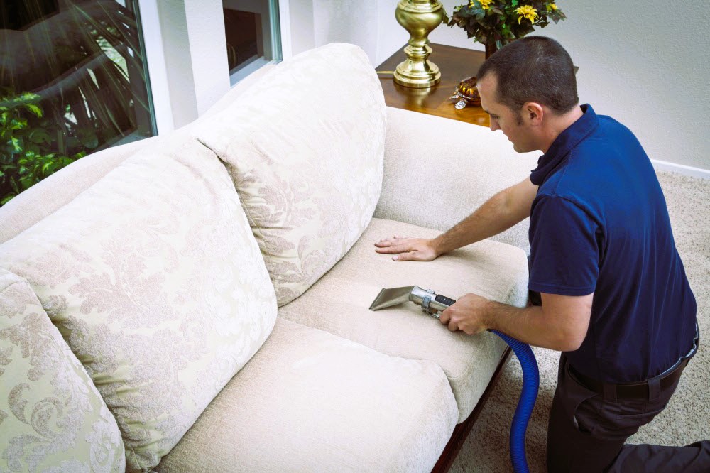 Man cleaning the sofa with a vacuum cleaner